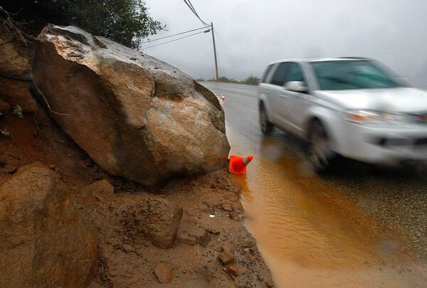 Loosened by the rain, a car-size boulder sits on the shoulder of Highway 79 just outside of Julian, Calif. County workers were kept busy clearing rocks and mud from roads in rural San Diego County. At higher elevations, they were clearing snow. See full story