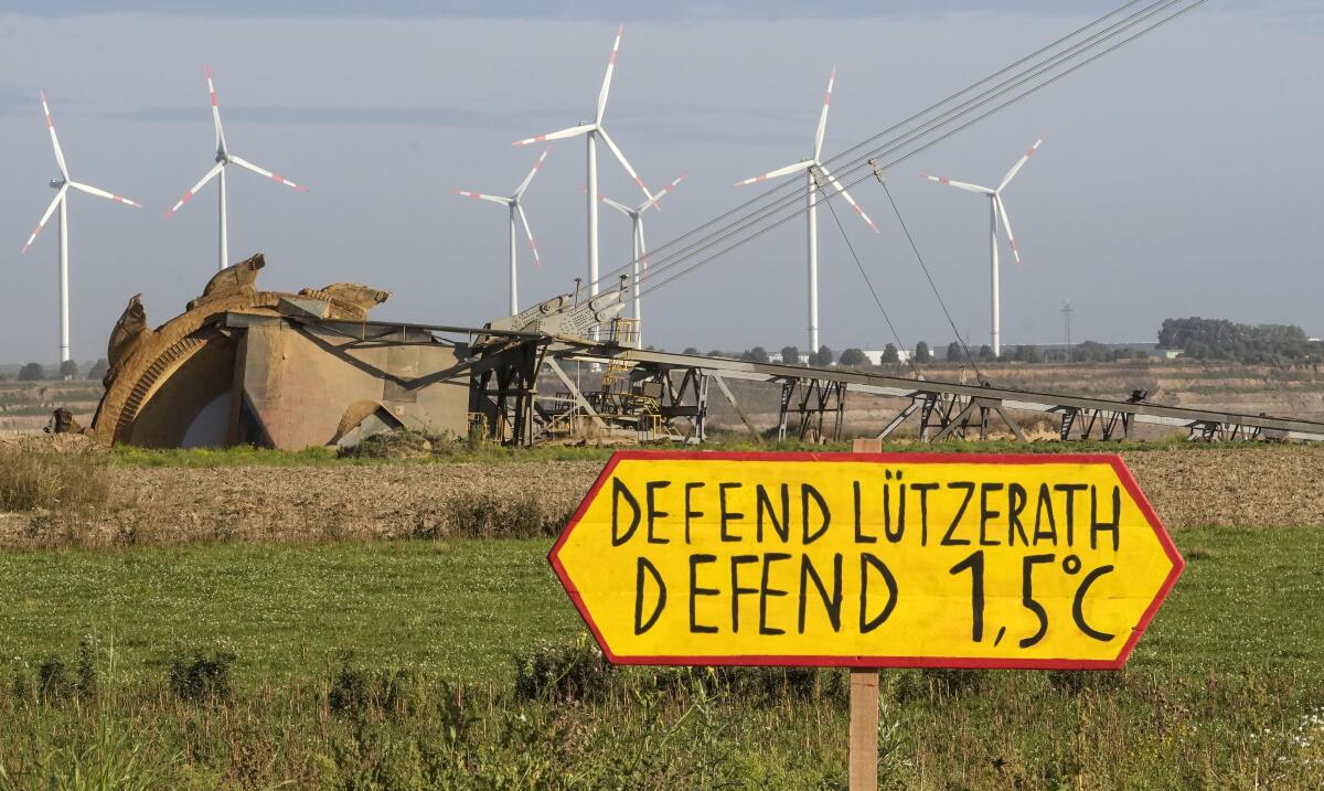 Climate activists protest against the Garzweiler open-cast coal mine with a sign reading "defend Luetzerath" in Luetzerath, western Germany, Friday, Oct. 1, 2021. The village of Luetzerath, now almost entirely abandoned as the mine draws ever closer, will be the latest village to disappear as coal mining at the Garzweiler mine expands. (AP Photo/Martin Meissner)