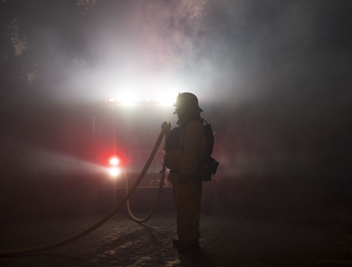 A firefighter holds a hose amid the Carmel fire near Carmel Valley, Aug. 18, 2020. 