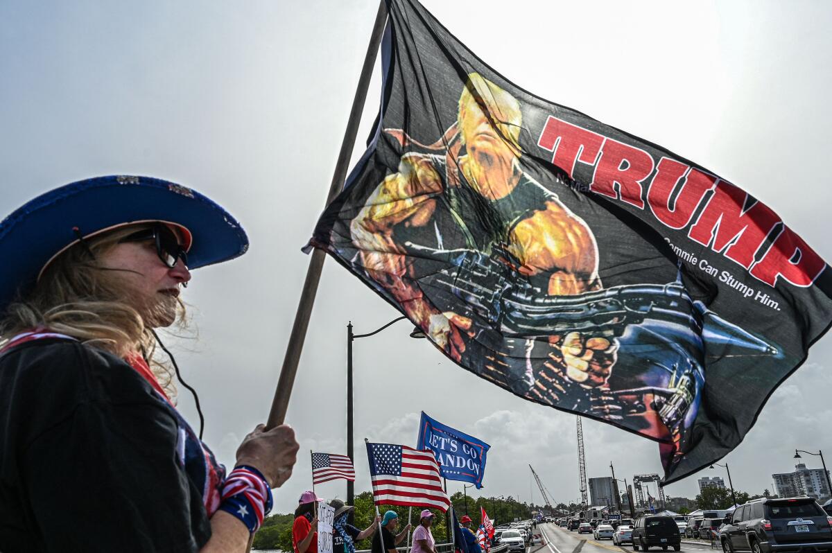 A woman holds a flag with "Trump" in large letters and a caricature of the former president 