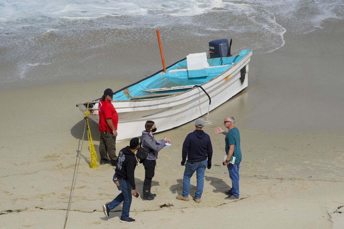 Investigators near the Children’s Pool in La Jolla look over a small boat on the beach used in a smuggling attempt.