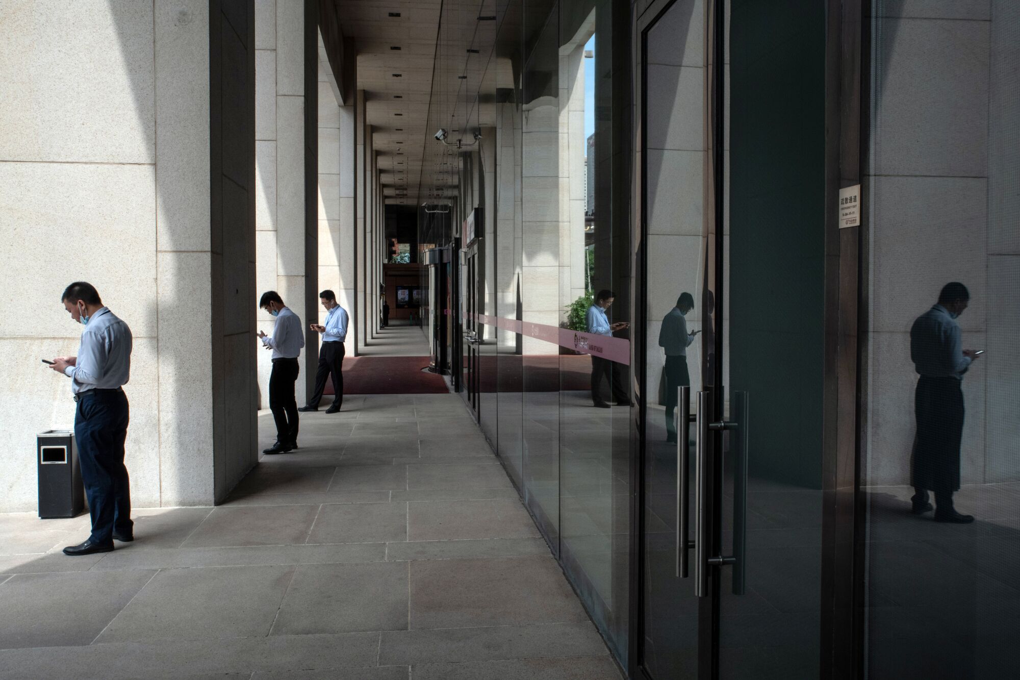 Office workers stand apart, looking at their phones.