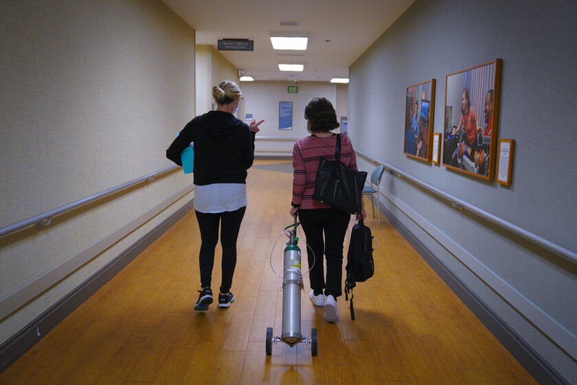 San Diego, CA - February 18: At the Sharp Allison deRose Rehabilitation Center at Sharp Memorial Hospital on Friday, Feb. 18, 2022 in San Diego, CA., Carolina Nieto, 63 walks with Suzanne Pruitt, Respiratory Therapist to work on breathing exercises. Nieto was diagnosed with COVID back in 2020 and still moves about her day with the help of oxygen. (Nelvin C. Cepeda / The San Diego Union-Tribune)