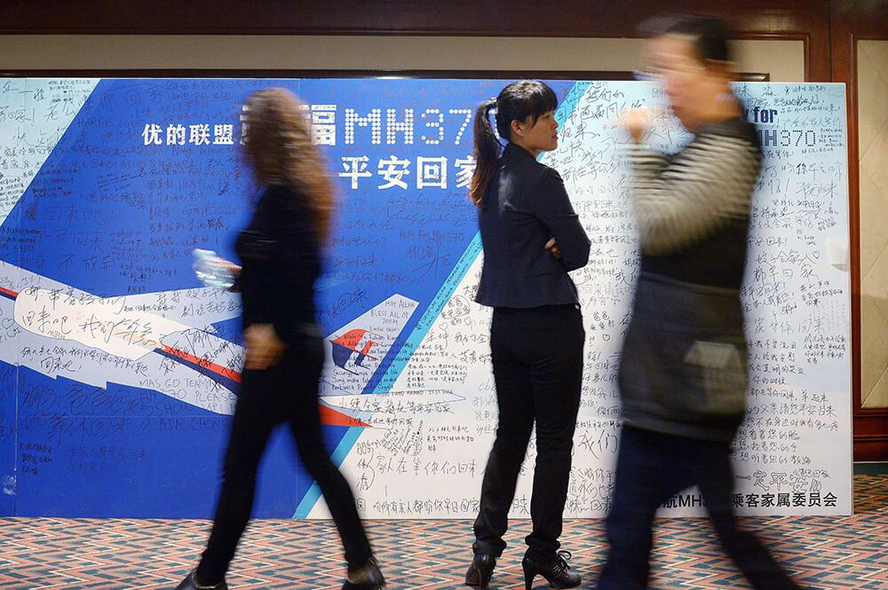 People walk past a billboard in support of missing Malaysia Airlines flight MH370 as Chinese relatives of passengers on the missing flight have a meeting at the Metro Park Hotel in Beijing on April 23.