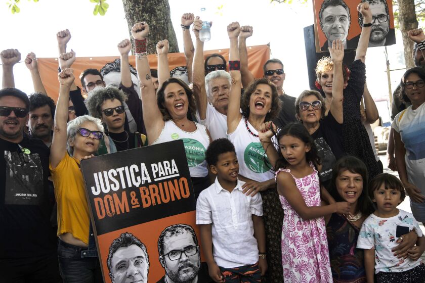 The relatives of British journalist Dom Phillips and activists hold a large poster with his image, left, and that of Indigenous activist Bruno Pereira, with the Portuguese message: "Justice for Dom and Bruno" at the one-year anniversary commemoration since their murders, in Rio de Janeiro, Brazil, Monday, June 5, 2023. The two were were killed in the Amazon's Vale do Javari area. (AP Photo/Bruna Prado)