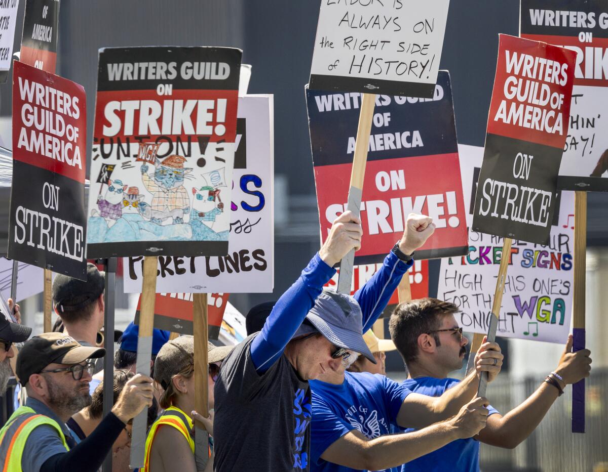 People hold up signs that say "Writers Guild on Strike!"