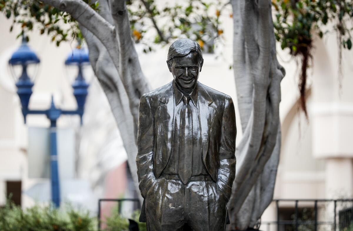 A bronze statue of a man in a suit is seen from a distance.