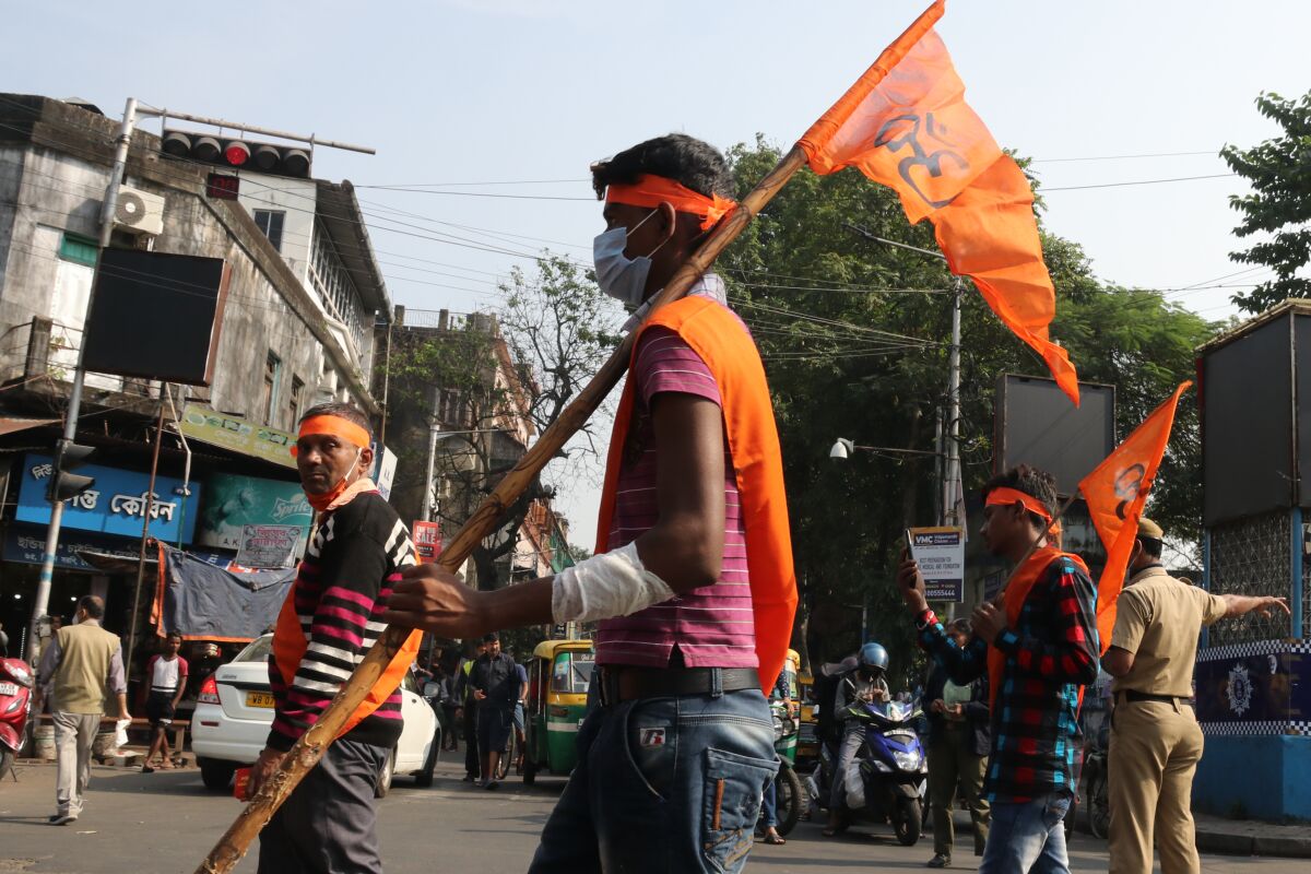 Three men in orange headbands and sashes stand amid traffic. Two are holding orange banners