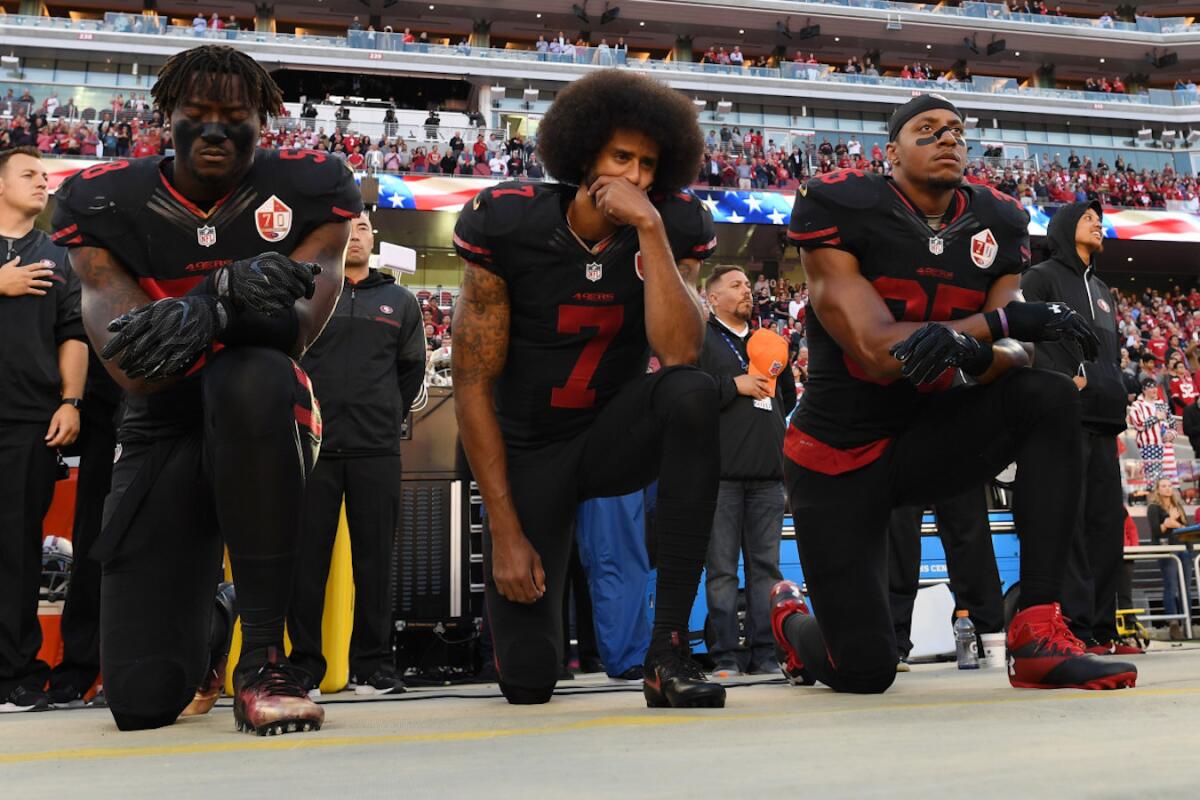 Eli Harold (i), Colin Kaepernick (c) y Eric Reid, de los San Francisco 49ers, protestan en la entonación del himno de EEUU en un juego de la NFL.
