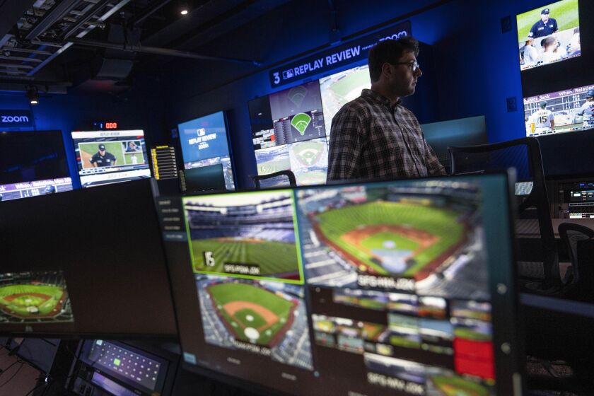 An employee walks past screens displaying gameplay clips at a Replay Review station during a tour at Major League Baseball headquarters in New York, Tuesday, March 28, 2023. (AP Photo/John Minchillo)