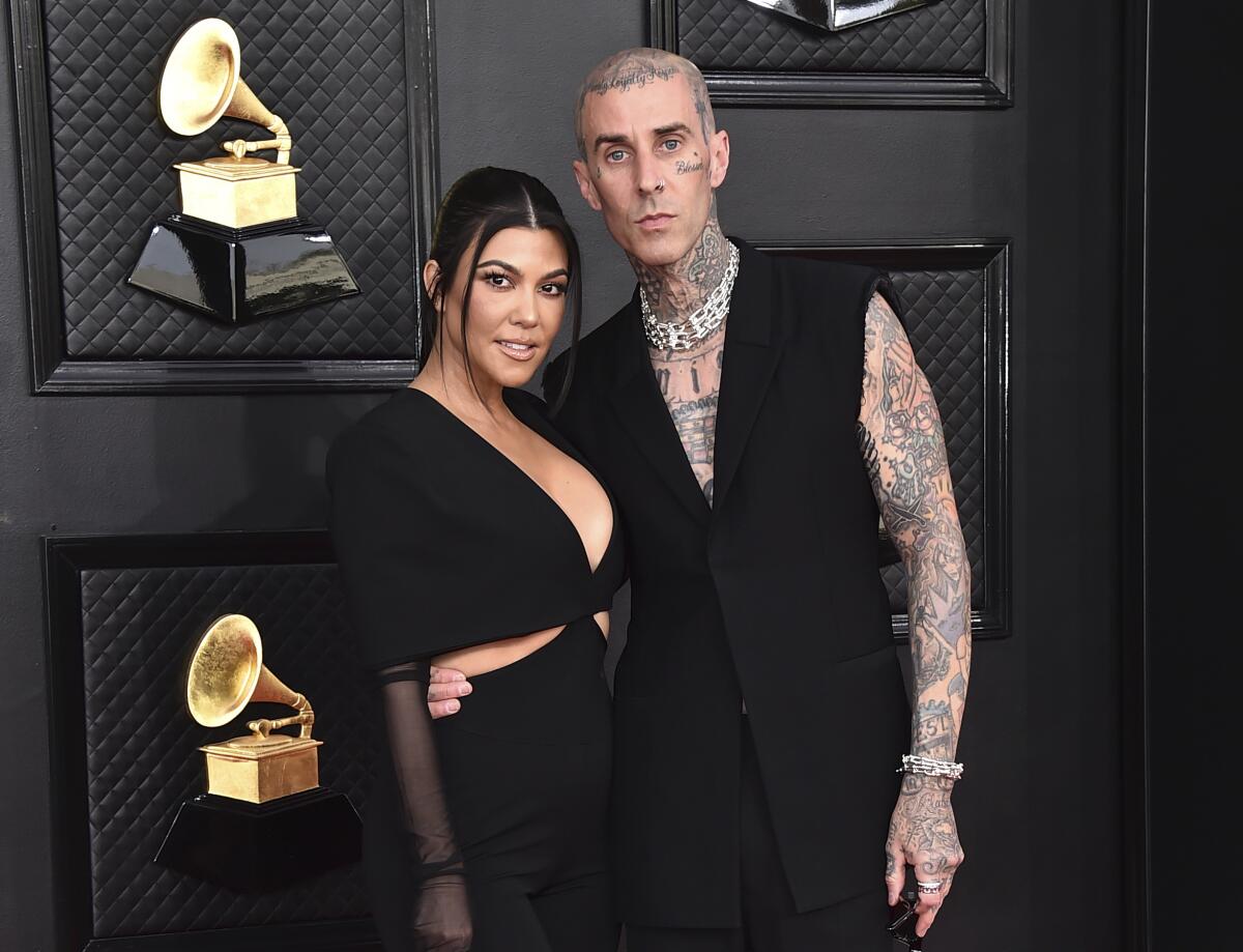 A heavily tattooed Travis Barker poses with his arm around Kourtney Kardashian's waist before an awards show