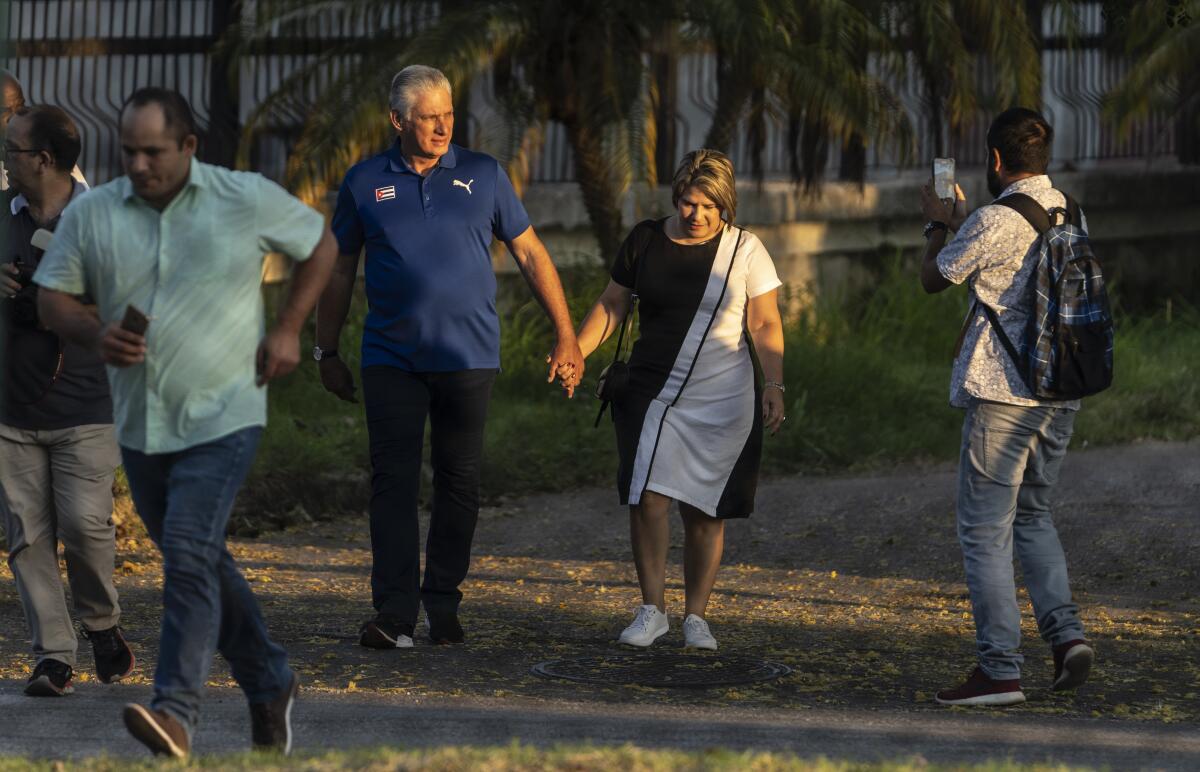 Visto a través de una valla, el presidente de Cuba, Miguel Díaz-Canel, camina con su esposa Lis Cuesta Peraza 