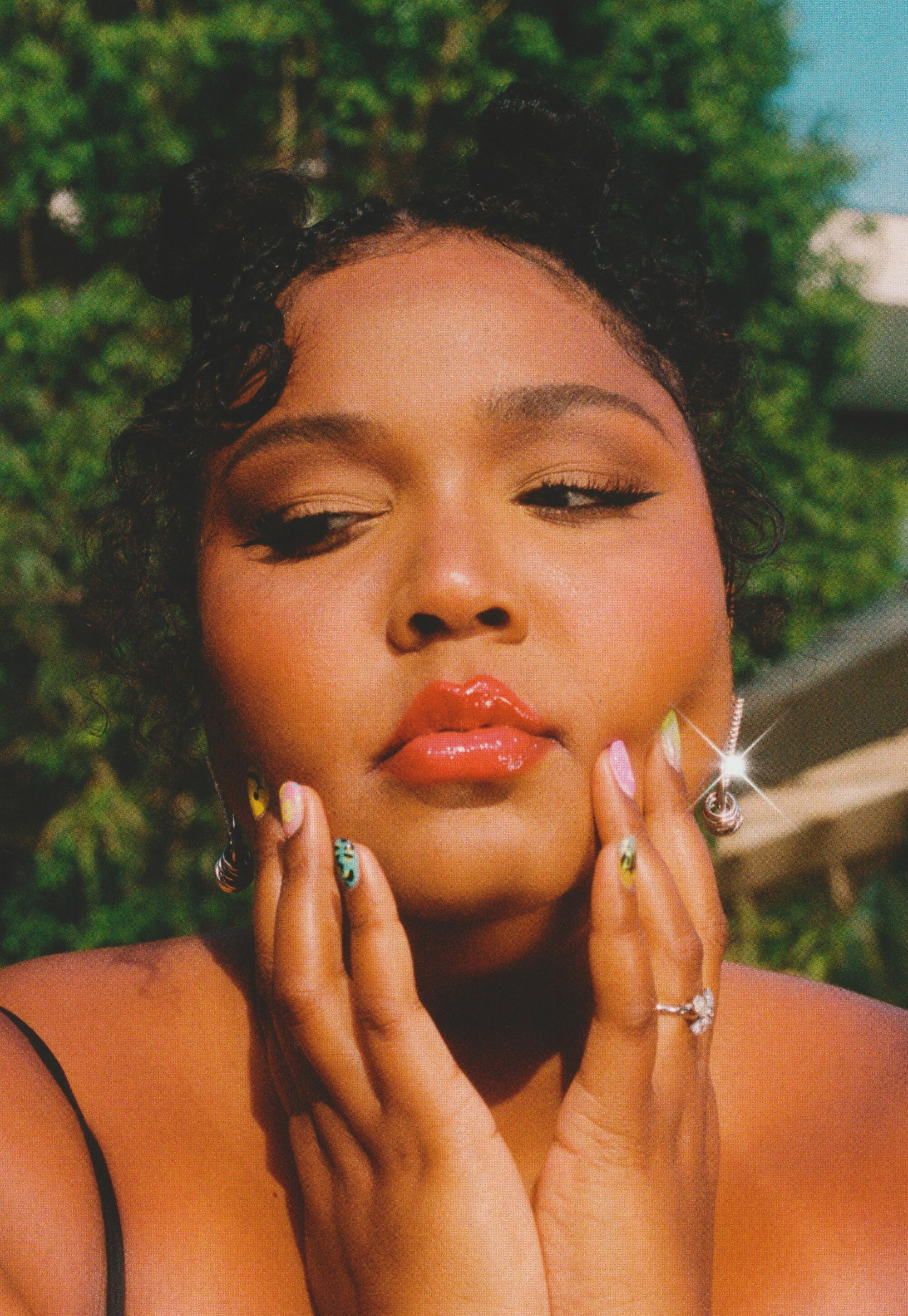 A woman with colorful nails and bright lipstick places her hands on her cheeks.