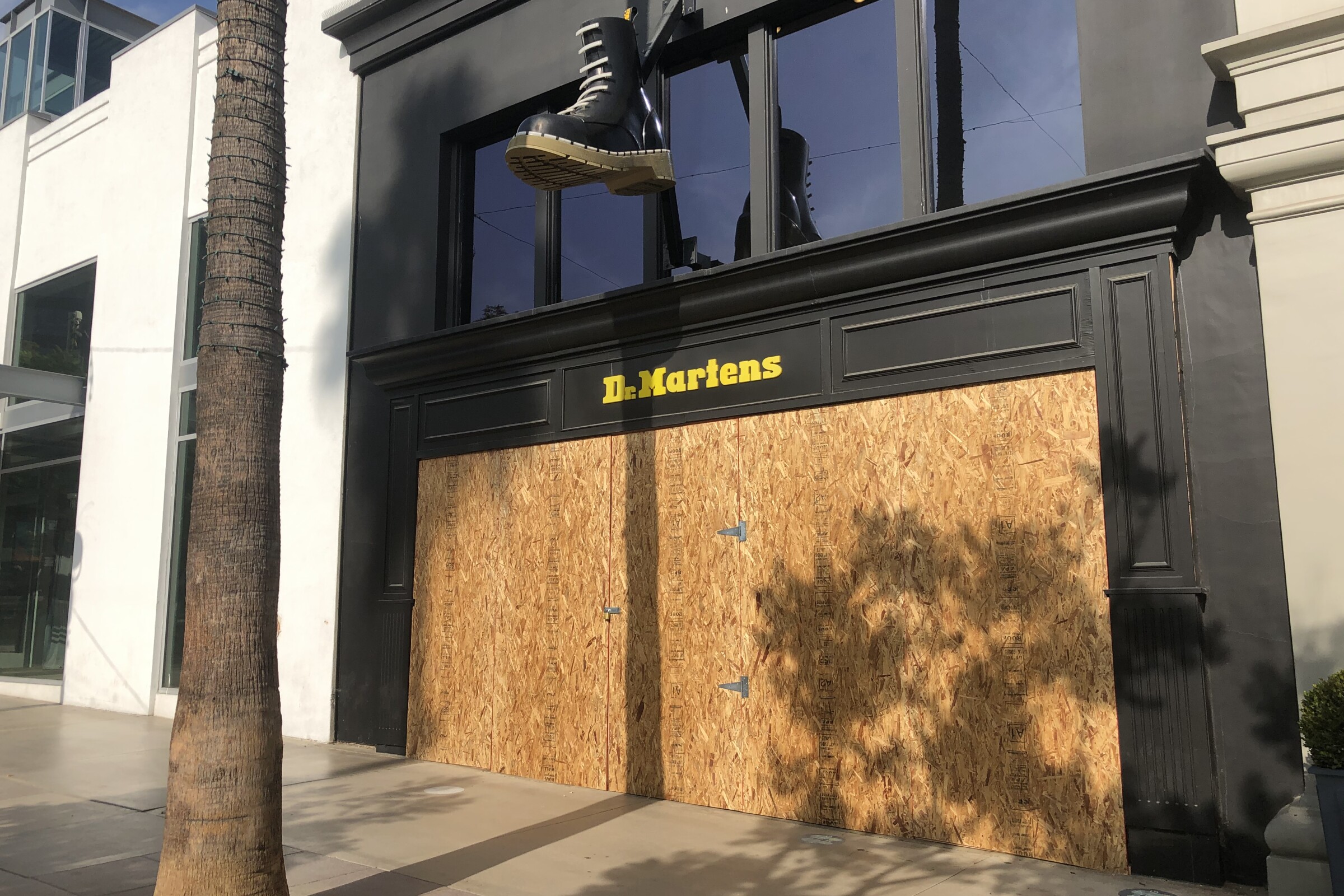 A giant Doc Martens boot hangs over a boarded up store on a pedestrian promenade
