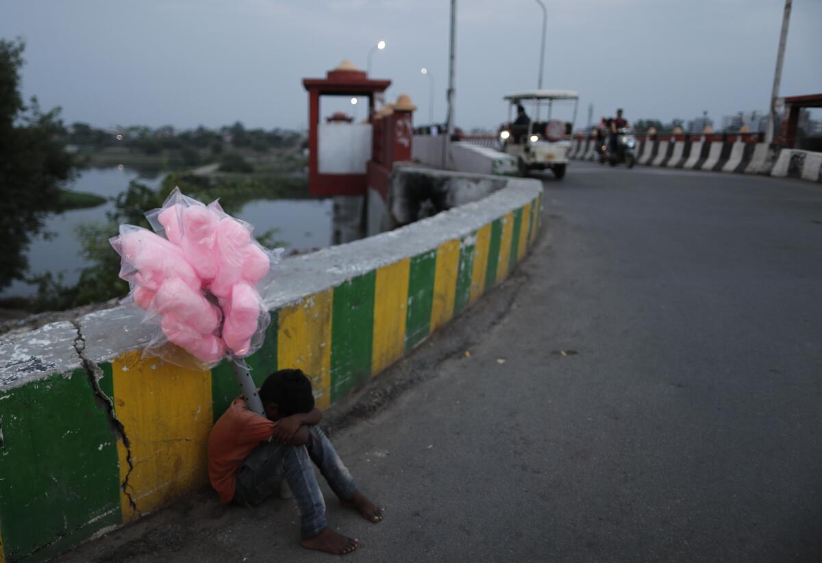 A young street vendor selling cotton candy lays his head on his knees sitting by a road 