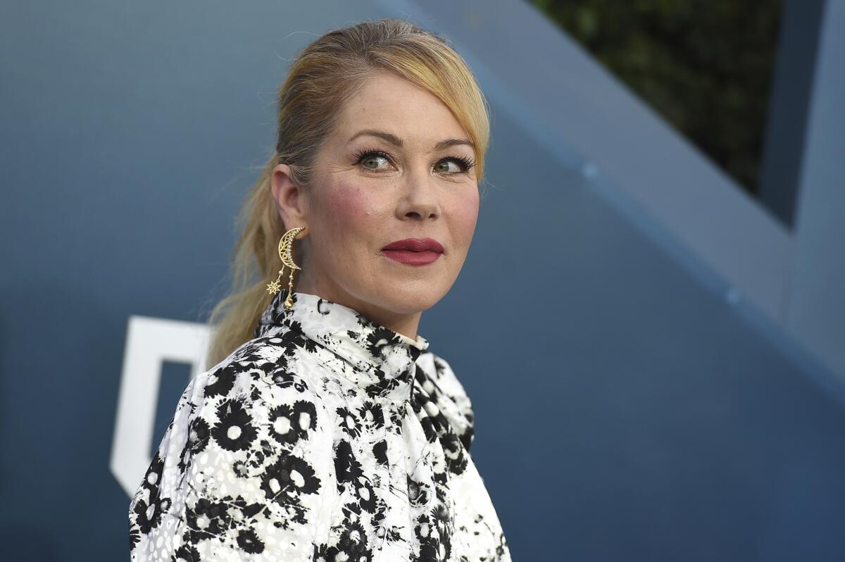 Christina Applegate, in black and white gown, stands in front of a blue backdrop