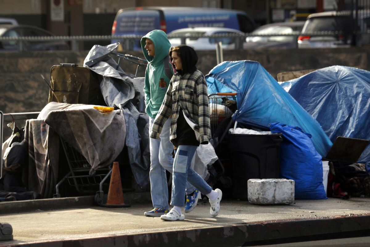 People walk past a homeless encampment.