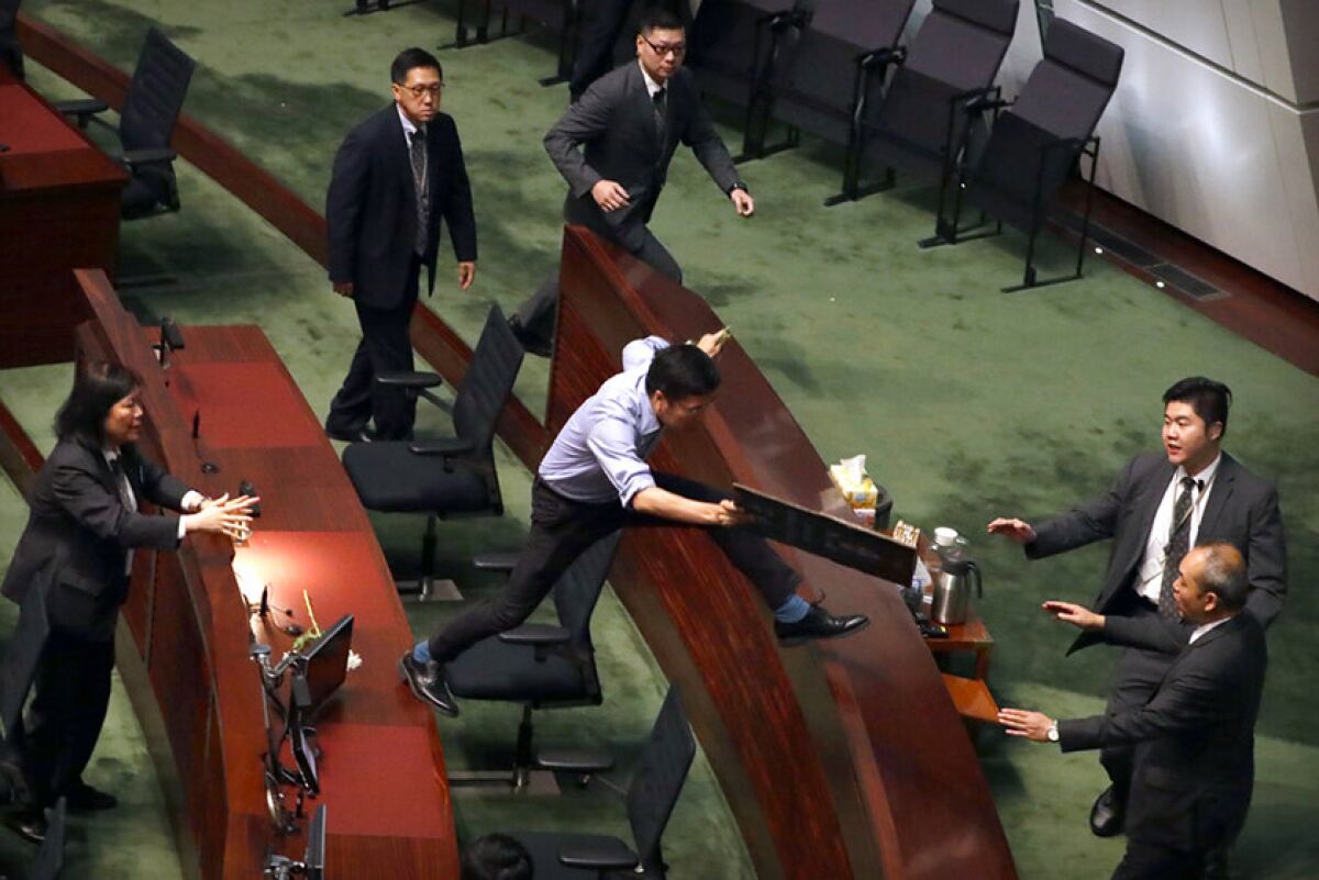 Security officers pursue pro-democracy lawmaker Au Nok-hin, center, as he leaps across desks at the Legislative Council in Hong Kong on Thursday. Nok-hin was chasing leader Carrie Lam as Lam left a question and answer session with lawmakers.