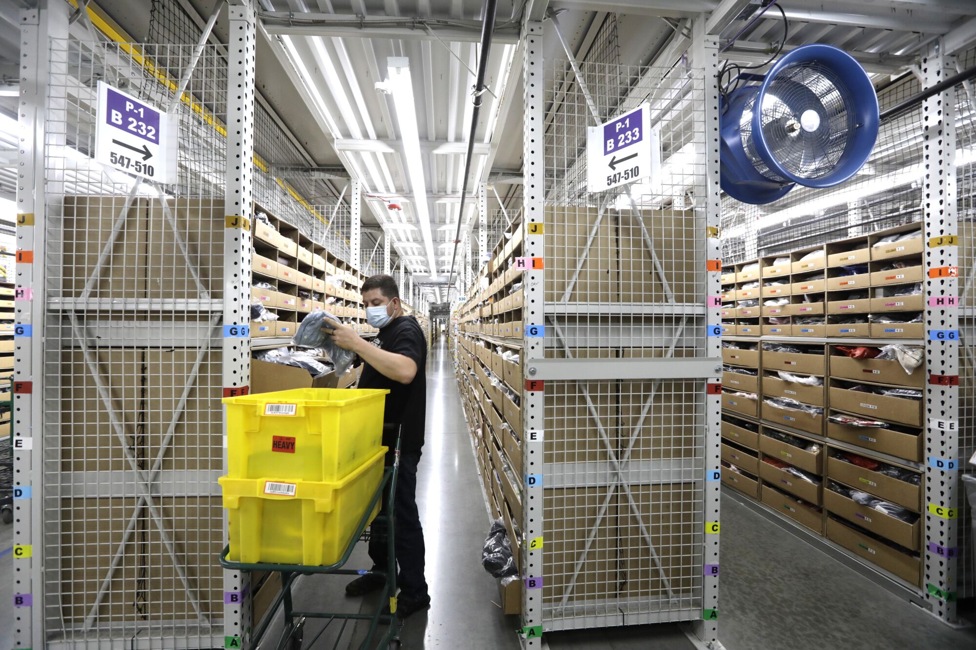 A warehouse worker handles merchandise next to two yellow bins