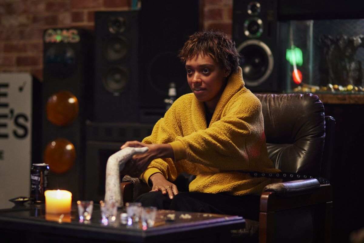A woman sits on a couch holding what looks like a sculpture of a hand.