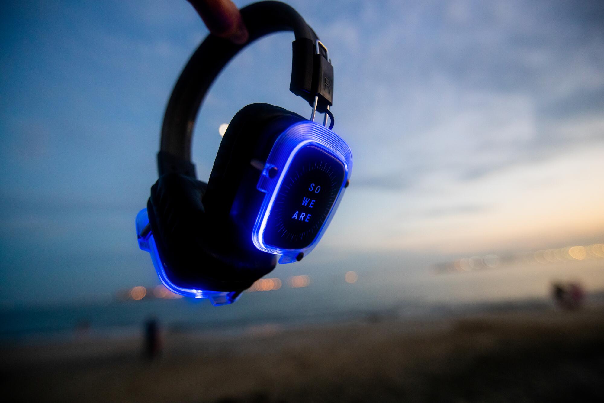 A detail image of glowing blue headphones used for silent disco dances, inscribed with the words "So We Are."