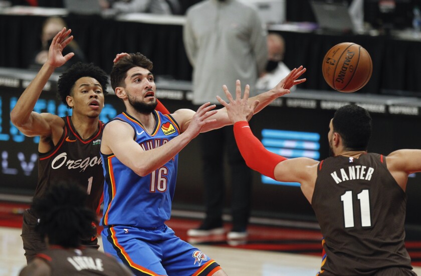 Oklahoma City Thunder guard Ty Jerome, center, passes as Portland Trail Blazers guard Anfernee Simons, left, and center Enes Kanter, right, defend during the first half of an NBA basketball game in Portland, Ore., Saturday, April 3, 2021. (AP Photo/Steve Dipaola)