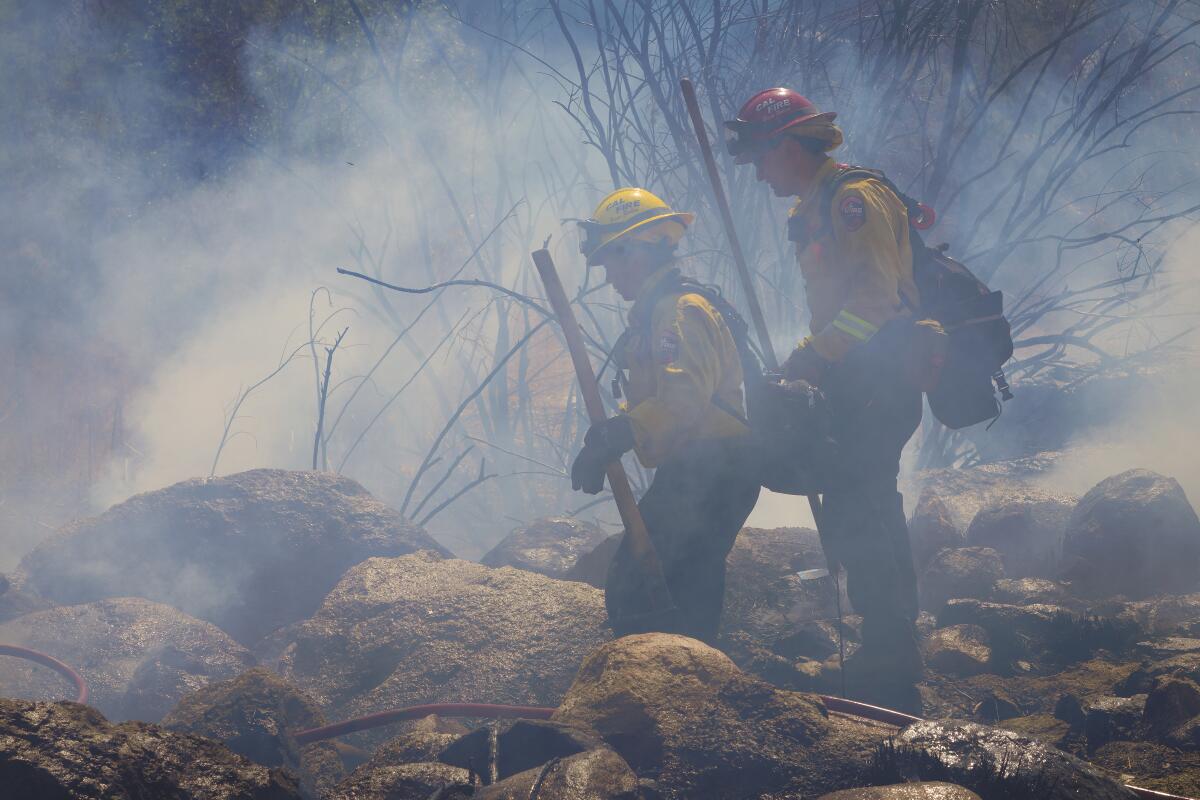 Two firefighters with hand tools stand in a smoldering area
