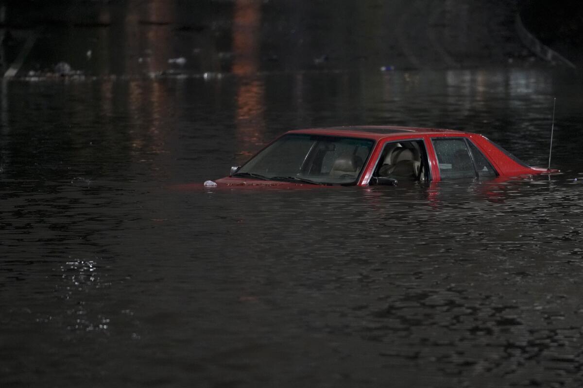 An empty vehicle is surrounded by floodwaters on a road.