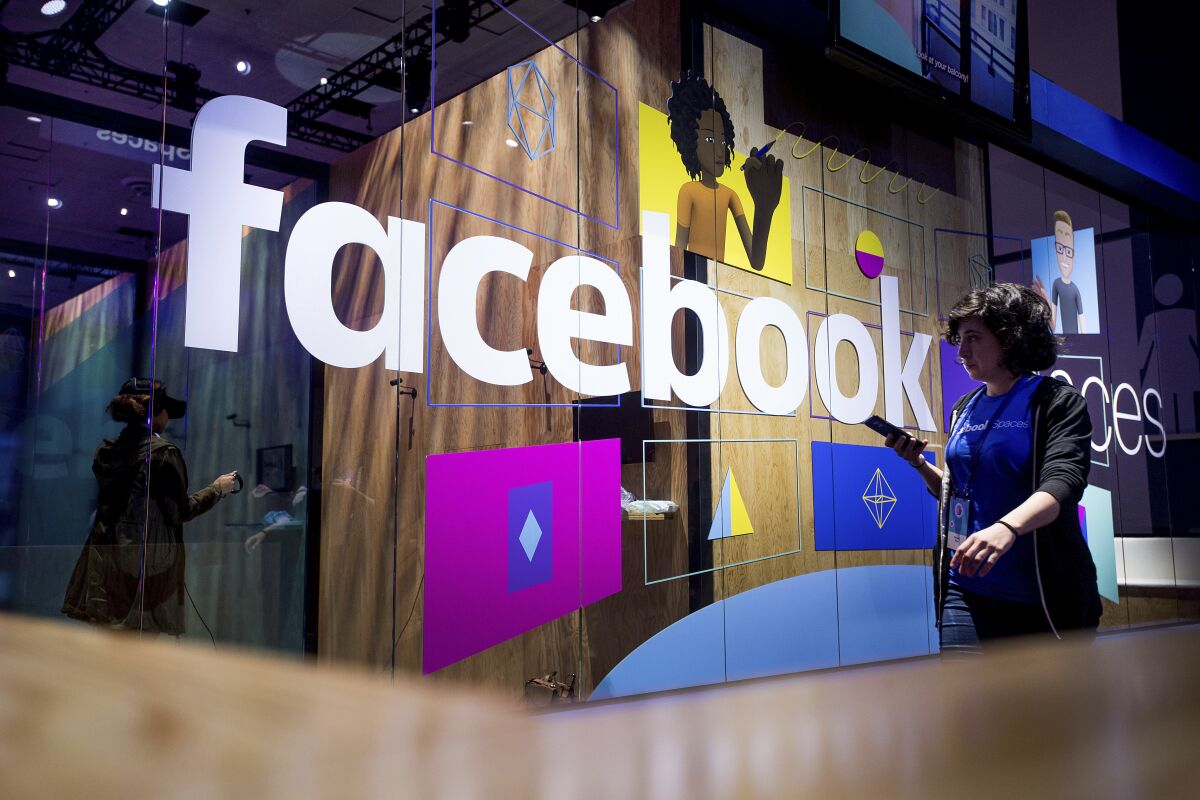 In this April 2017, photo, a conference worker passes a demo booth at Facebook's annual F8 developer conference in San Jose. 
