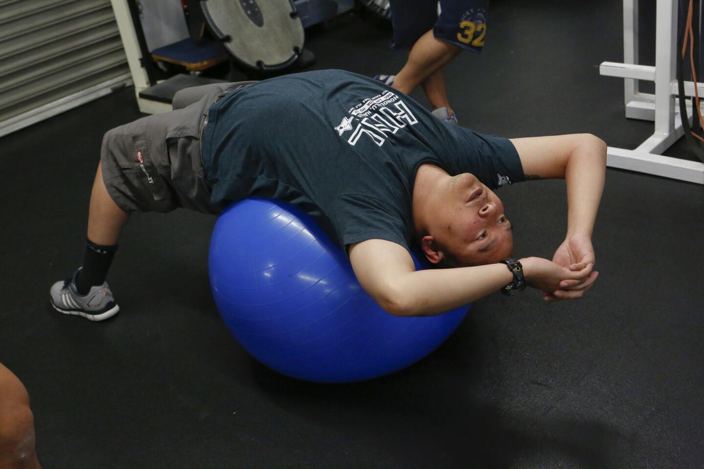 Culver City police officer Tri Lai stretches on a ball at A Tighter U gym in Culver City. Li, a member of the Culver City police force for 15 years, was seriously injured in a 2013 motorcycle accident. After months in the hospital, he began training to return to work.