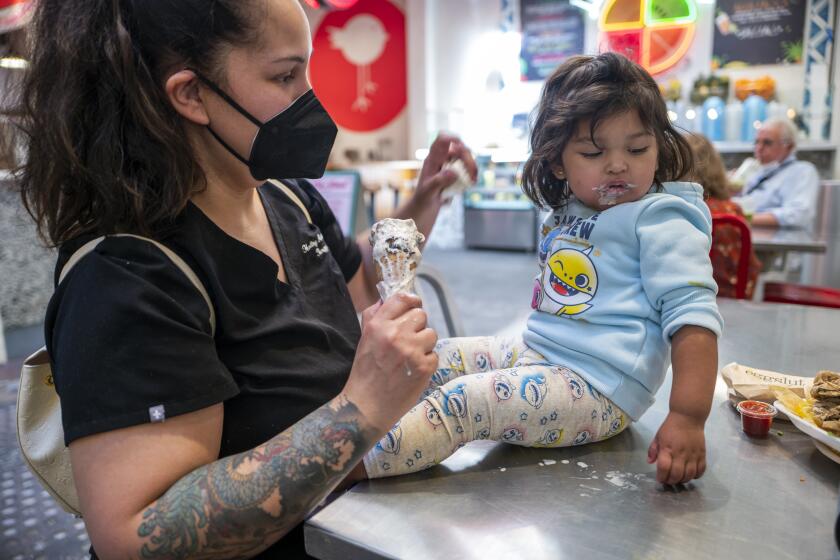 LOS ANGELES, CA - MARCH 01: Lucy Nevarez 30, left, and daughter Natalia Martinez, 2, right, are enjoying some ice cream at Grand Central Market on Tuesday, March 1, 2022 in Los Angeles, CA. Today more than half the customers were wearing masks at the market. California officials announced that face masks will no longer be required indoors starting Tuesday, as the state shifts to an "endemic" approach to the coronavirus. Masks will be "strongly recommended" for unvaccinated people in most indoor settings like shops, gyms, bars and movie theaters, but they will no longer be mandated by the state after Tuesday. (Francine Orr / Los Angeles Times)
