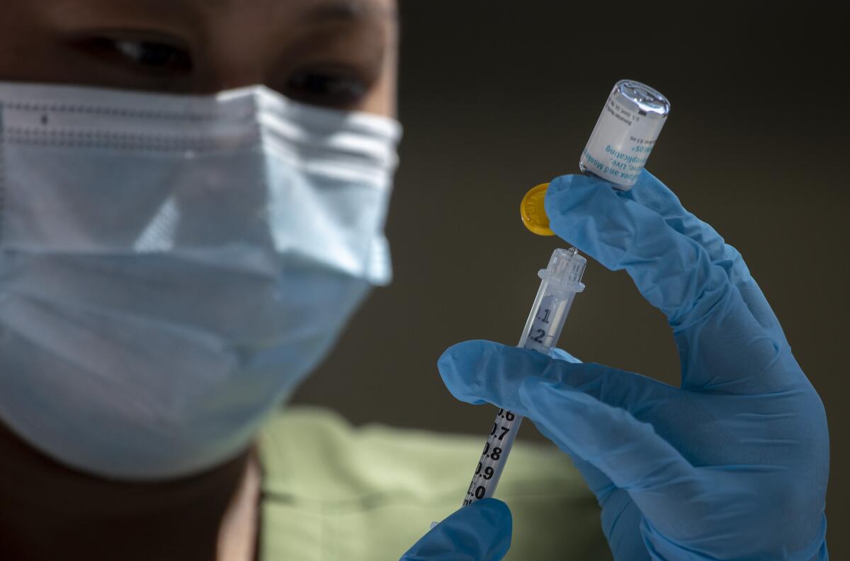 A masked and gloved person puts a needle into a vial.