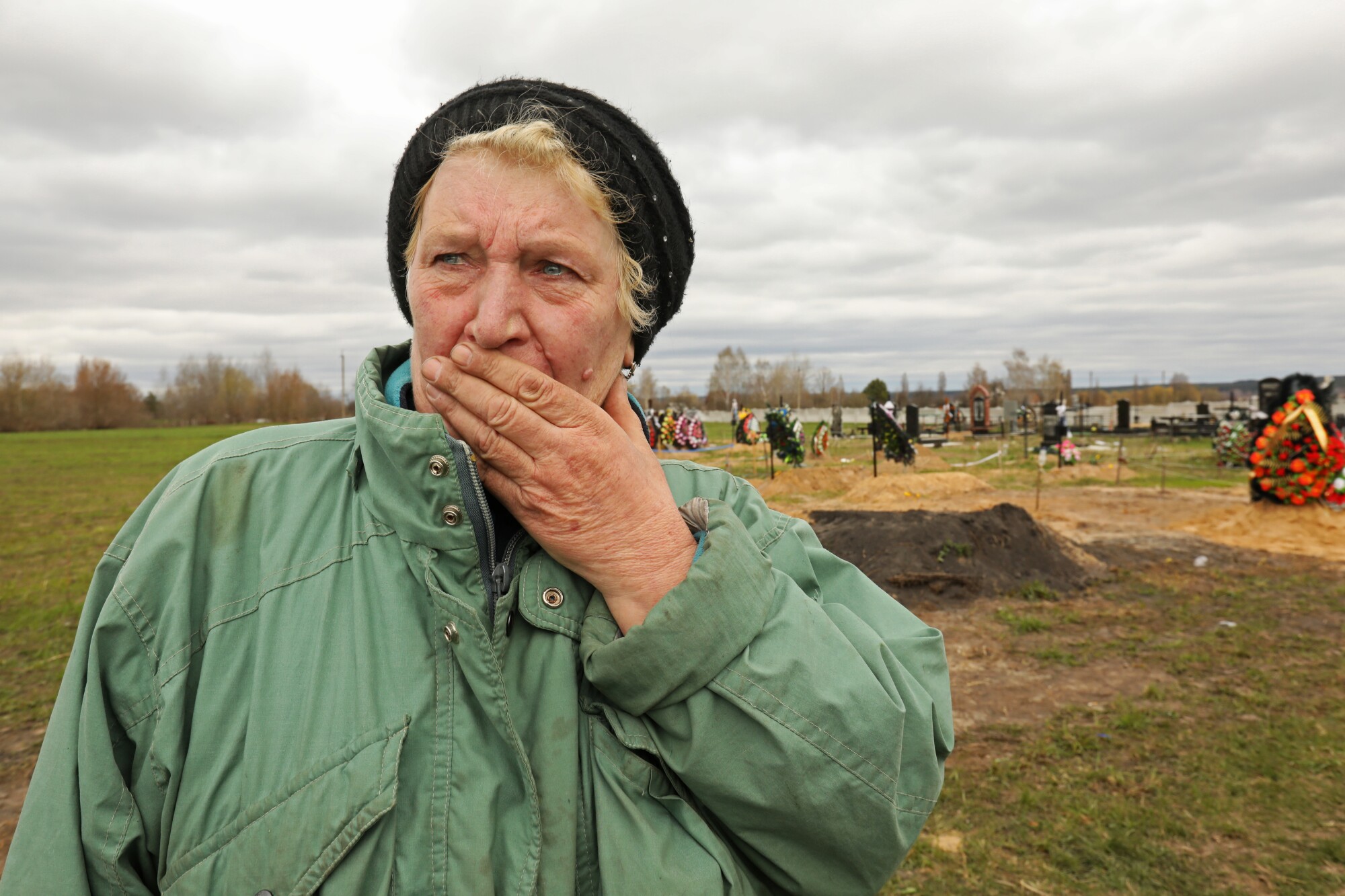 A woman covers her mouth with her hand standing in front of a mass gravesite