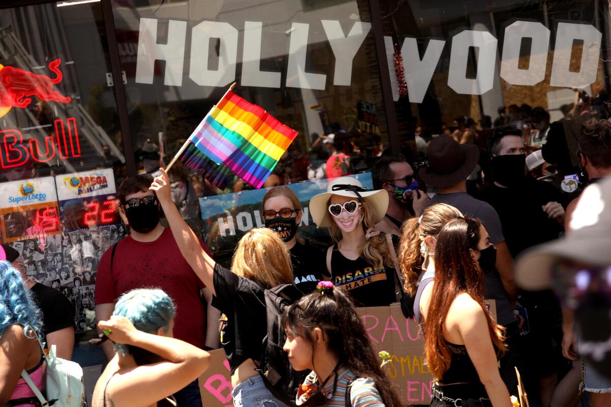 A person in a crowd holds up a rainbow flag with the word Hollywood behind them