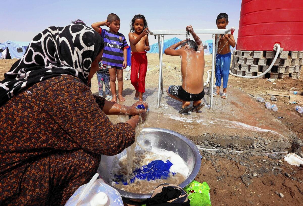 An woman washes her family's laundry as the children shower outside their tent at a temporary camp for civilians fleeing violence in northern Iraq.