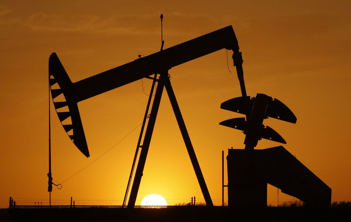 A pump jack is silhouetted against the setting sun