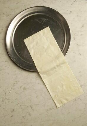 Brush a filo leaf with butter, fold it in half and lay it on a pizza pan, letting it hang over the side.