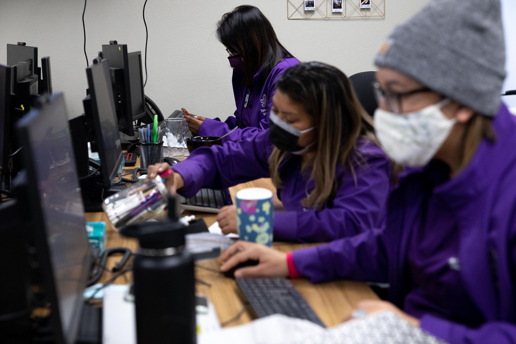 People in purple shirts sit at desks and type on computer keyboards.