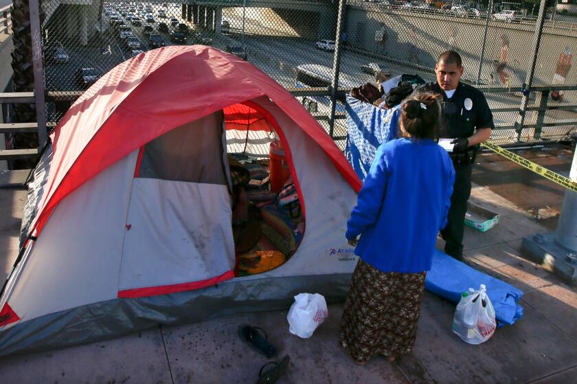 The city of Los Angeles has agreed to pay more than $800,000 to settle a lawsuit over the confiscation of homeless people's possessions. Above, a police officer talks with a homeless woman on a downtown freeway overpass in March.