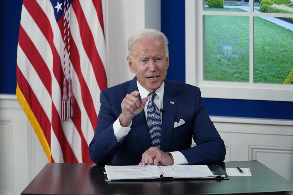 President Biden points as he speaks from a White House desk during a virtual summit.