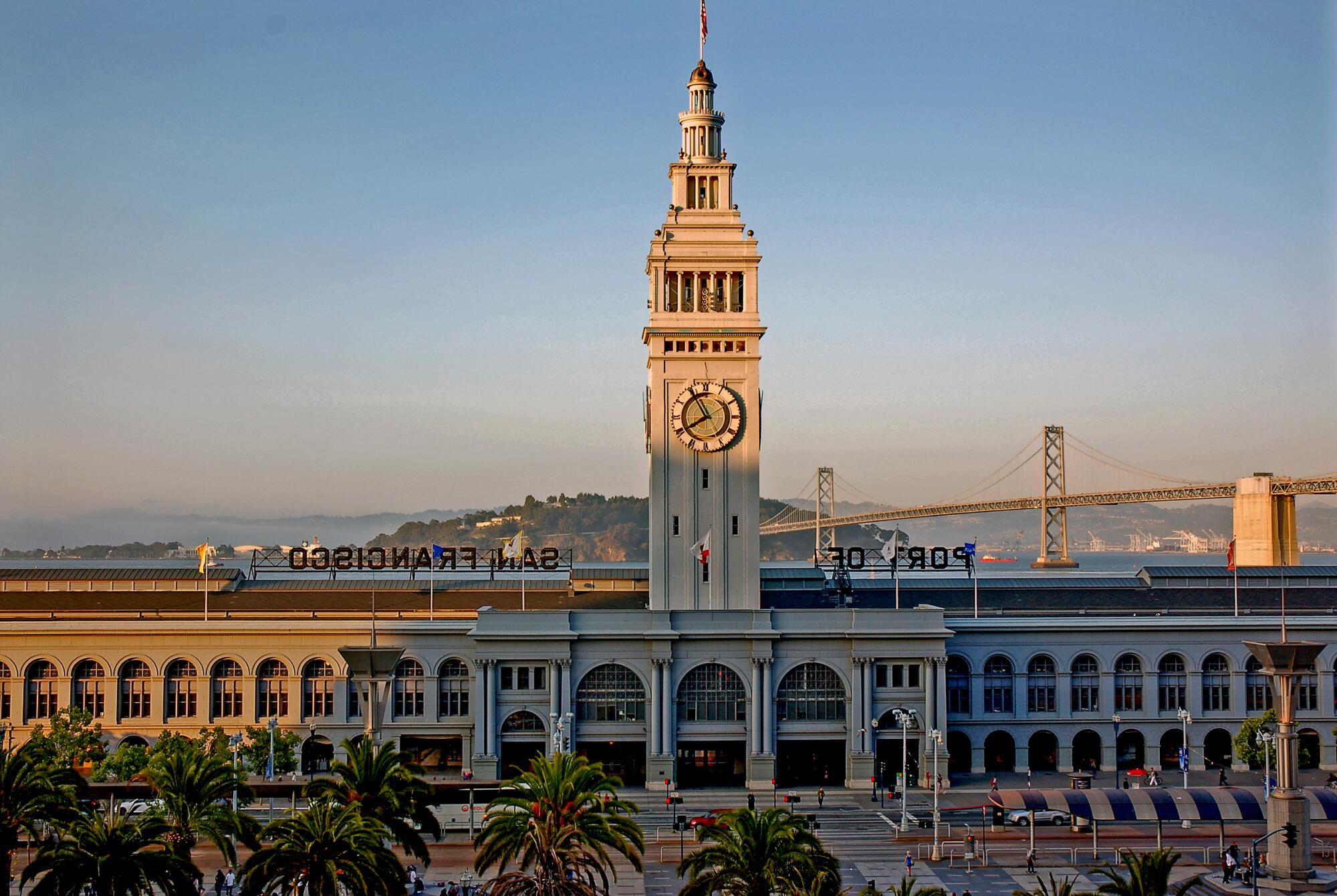 A building with a colonnade of arches and a tall clocktower, with the Golden Gate Bridge in the background.