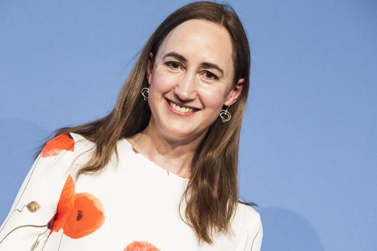 Author Sophie Kinsella smiles while wearing  a white dress with red blossoms on it