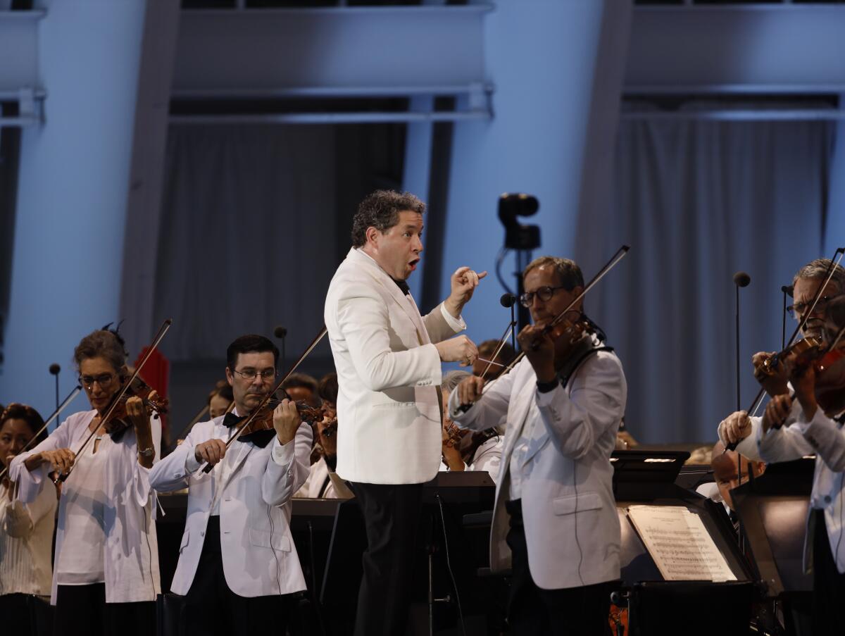 Gustavo Dudamel conducts in a white suit jacket.