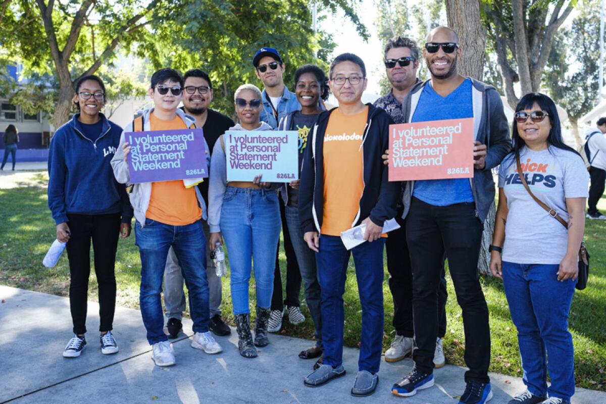 A group of volunteers with 826LA stand together smiling, with some holding up signs