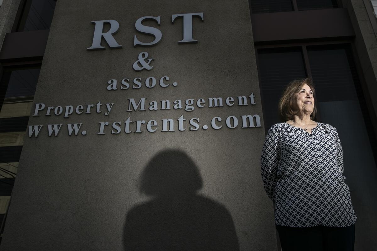 A woman stands in front of a sign that says "RST & Assoc. Property Management."