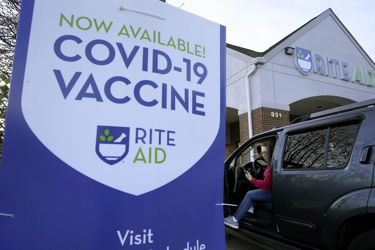 A woman steps out of her car near a COVID-19 vaccine sign at a Rite Aid pharmacy in Nashua, N.H. 