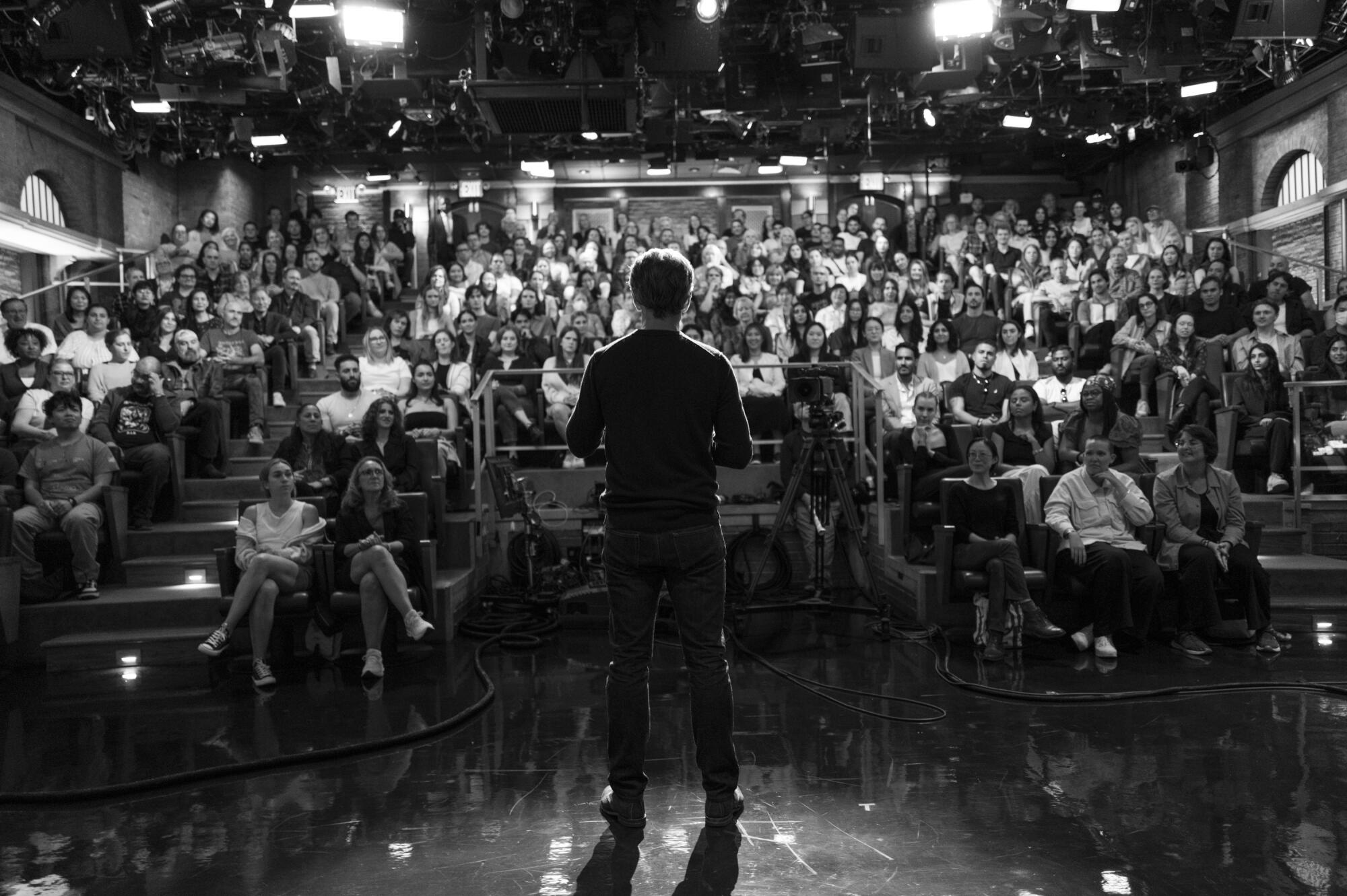 Seth Meyers as seen from behind as he faces a studio audience.