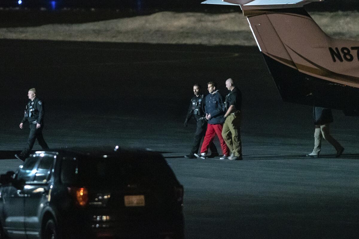 Law enforcement officials lead a handcuffed man from a plane on a dark airport tarmac.