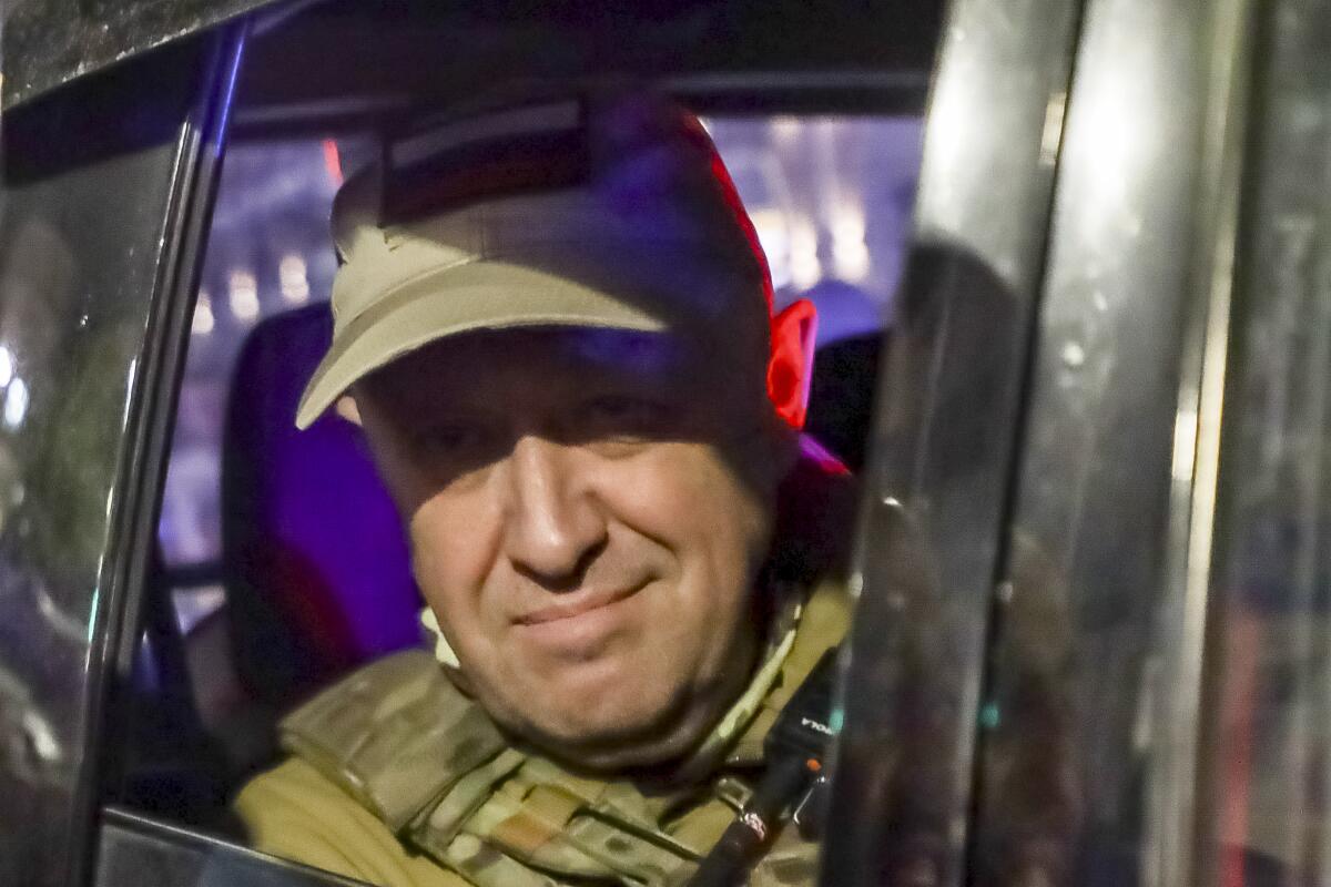 A man in a khaki cap and fatigues looks out from a military vehicle.