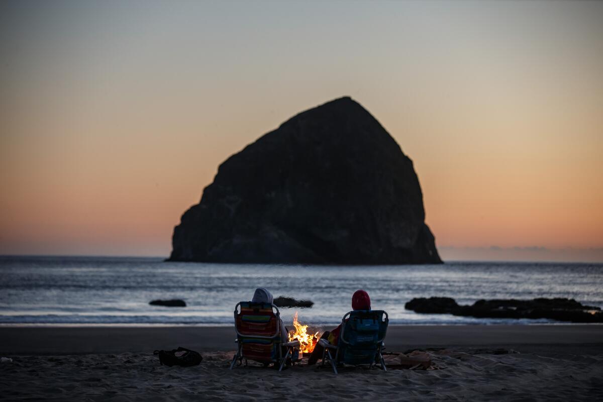 Samantha Hill, left, and Holly Battle, right, sit by a warm bonfire on the beach in Pacific City, Ore.
